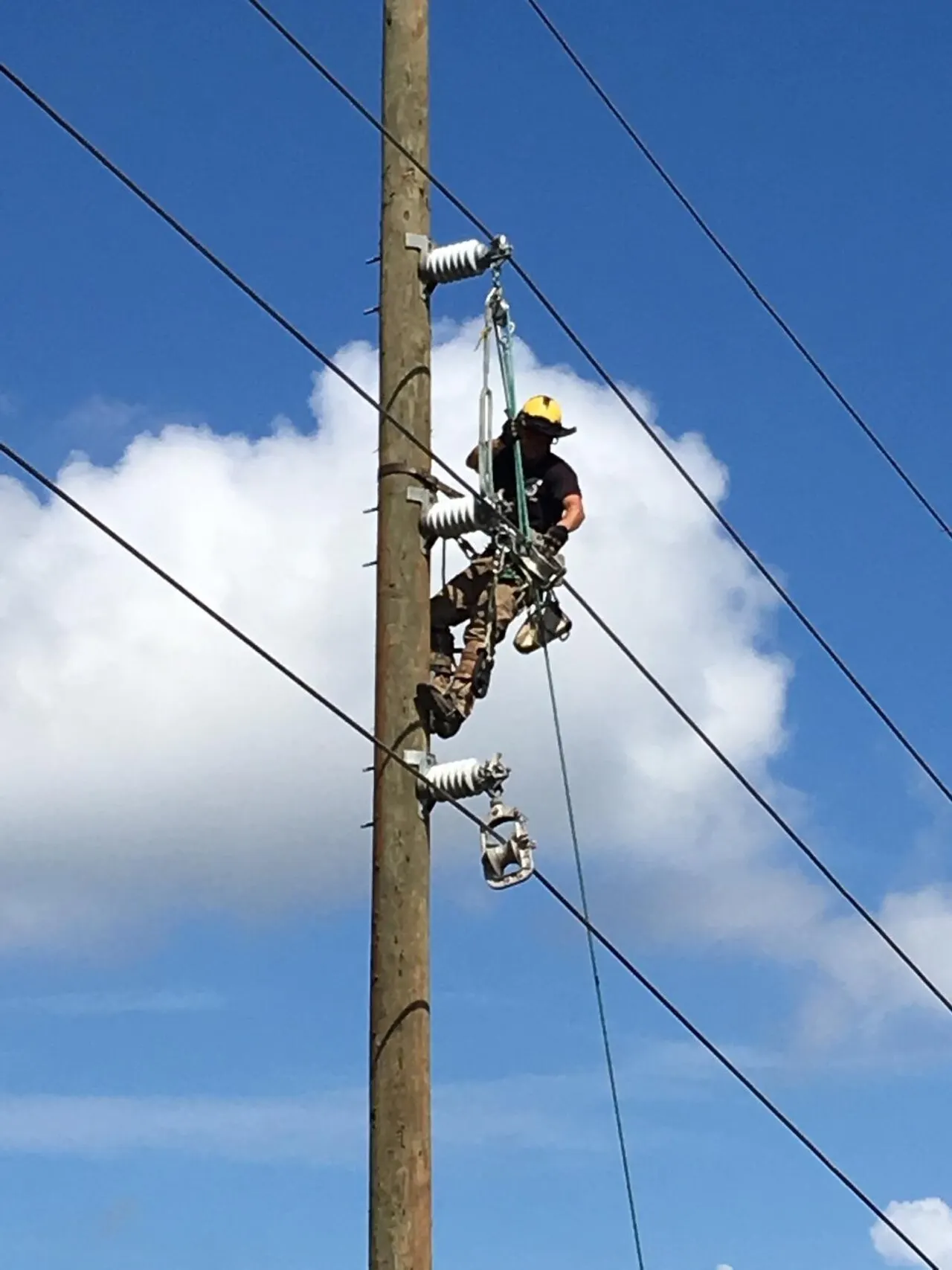 Electrical worker climbing a utility pole against a blue sky